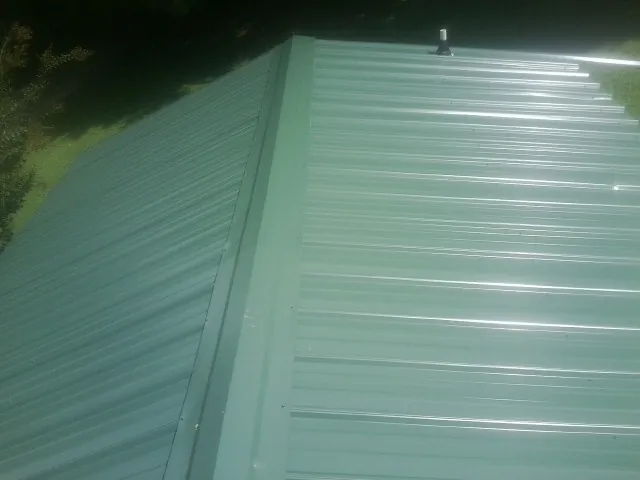 New green metal panels meeting at the ridge of a roof — Flat Roof Repair work by our crew in Hastings