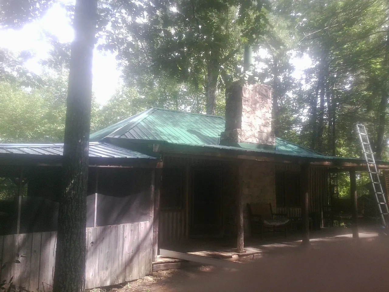 Green metal roof and stone chimney above a log cabin porch in Hastings