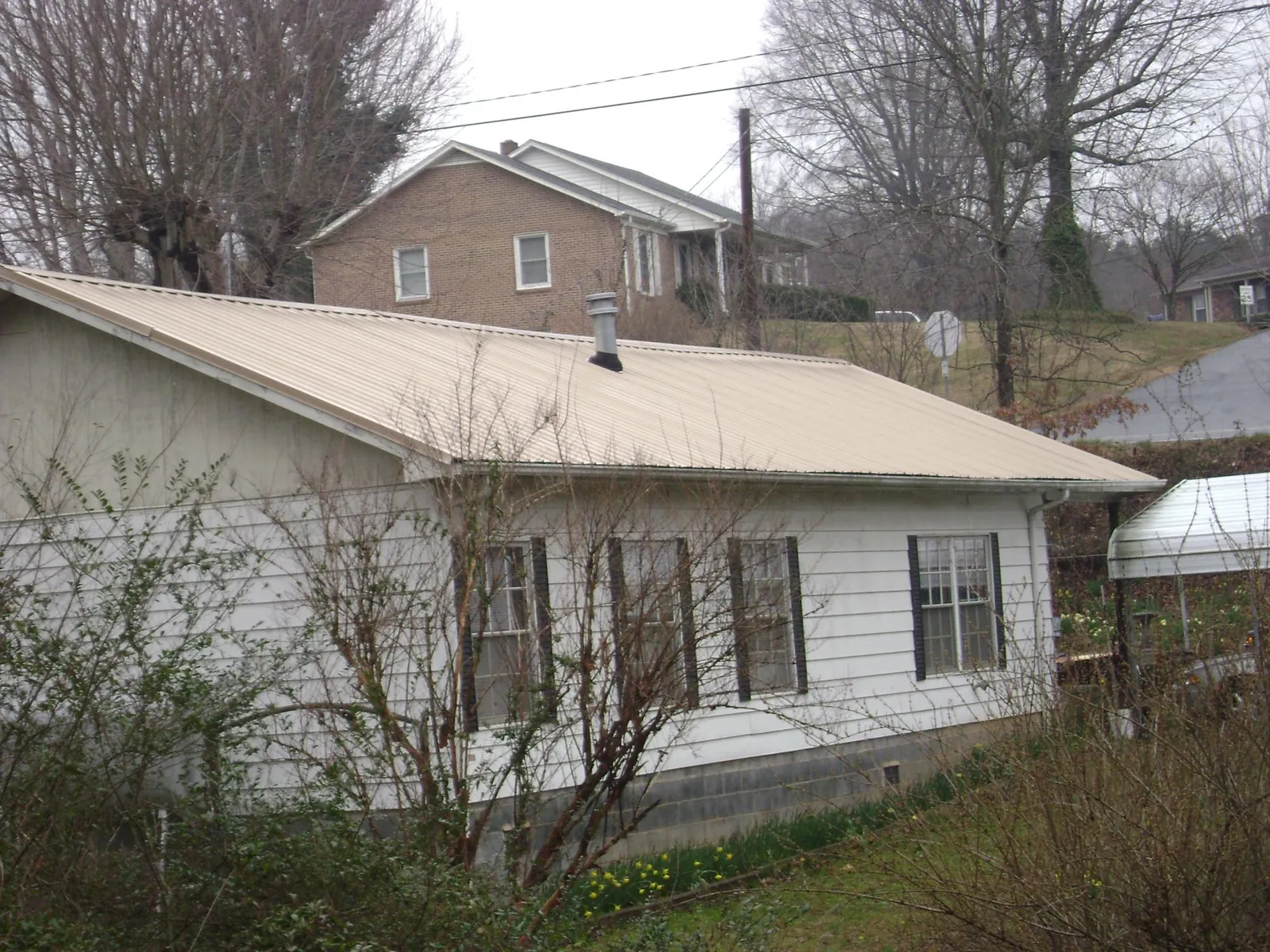 Tan metal roof on a white sided house set into a hillside — Commercial Roofing by Roofing Brothers in Hastings
